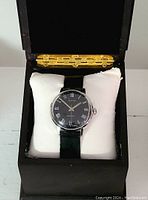 Front view of the vintage Alpine wristwatch with black dial inside a black box on a white cushion.