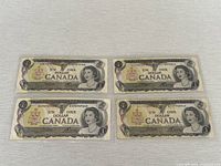 Four Canadian one dollar bills laid out in two rows of two, showing front face with Queen Elizabeth II and Canada coat of arms.
