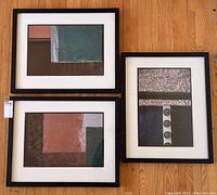 Three framed modern abstract photographs arranged on wooden floor showing varying geometric textured compositions and artist signatures.