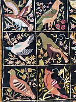 Close up of three columns of bird motifs embroidered in multicolor yarn on black background