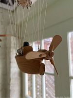 Side view of one wooden flying machine sculpture showing the propeller, canvas sail and suspension strings.