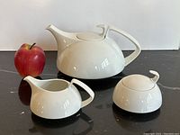 Group shot of teapot, creamer, sugar pot with apple for scale