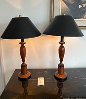 Full view of both turned wood lamps with shades on black tabletop