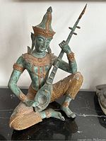 Front-left view of seated deity statue on black surface against white wall