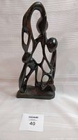 Front view of the dark wooden abstract sculpture showing flowing carved figures on a flat rectangular base.