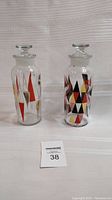 Two vintage mid-century modern apothecary jars with geometric triangle designs on clear glass, each with a faceted glass stopper lid, standing side by side.