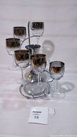 Front view of the decanter and six smokey silver-tinted stemmed glasses arranged on a metal stand.