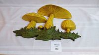 Three yellow mushrooms with green grass base wall sculpture shown from the front on a white background with lot number.