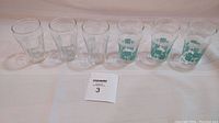 Six vintage juice glasses grouped in one image on a white surface, showing all glasses and a card with the lot number.