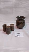 Lot shows one vase and three small shot glasses on a white fabric surface