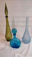 Full set of three vintage Empoli glass decanters of various colors and styles displayed on a white background.