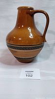 Front view of the vintage brown glazed German pottery pitcher showing the handle and decorative band on the body.