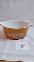 Photo showing front side of vintage Pyrex Butterfly Gold casserole dish with floral and butterfly pattern on mustard yellow exterior and white interior.