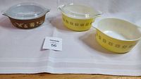Three Pyrex casserole dishes: on the left, brown "American Harvest" pattern with lid; middle and right yellow dishes in "Town and Country" pattern, one with lid and one without.
