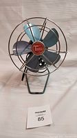 Front view of vintage Torcan fan showing blue metal blades and chrome protective cage with red Torcan branded center hub.