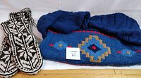 Photo of blue handmade wool sweater with geometric patterns laid flat next to tall black and white patterned wool slippers.