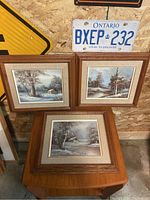 Set of three framed oil paintings arranged on and against a wooden surface showing matching frames and beige linen matting