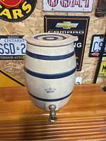 Front view of stoneware crock showing body, blue bands, crown emblem, and metal spigot