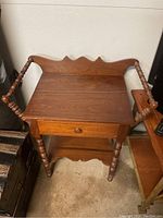 Front view of the antique wooden wash stand showing the carved backboard, turned spindle side rails, and drawer.