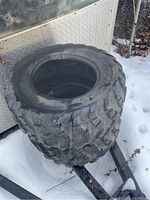 Photo showing two stacked Maxxis ATV tires outdoors on snow, showing overall size and tread.