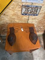 Two large rust-colored metal bumble bee shaped candle holders displayed on a wooden table against a wood paneled wall with a vintage license plate.