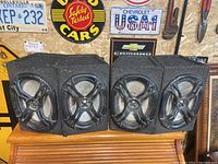 Front view of four rectangular speaker boxes covered in grey carpet with MTX 6x9 speakers and black grills inside showing dust accumulation.