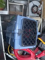 Blue plastic cat carrier with black diamond grid vented door, shown from side angle with door closed and latch visible.