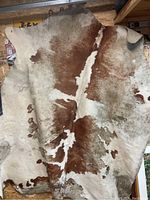 Full view of large cowhide rug with brown and white hatched pattern displayed hanging, showing natural shape and size.