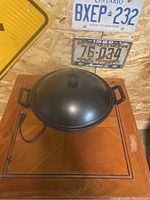 Electric wok with lid placed on wooden surface, with background of vintage license plates.