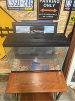 Front view of the empty rectangular glass fish tank with black hood and gravel inside