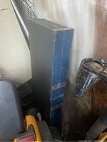 Folded picnic table standing upright showing worn blue metal exterior and latches for securing the fold mechanism.