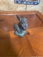 Gargoyle statue front and side views on wooden surface, showing detailed facial features and wings.