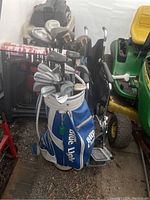 Full view of Blue Light branded golf bag filled with multiple golf clubs, standing upright next to a riding lawn mower.
