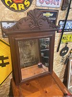 Full view of antique wooden framed mirror with detailed top hand carved design and glass mirror surface.
