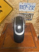 Front top angle view of Keurig 2.0 coffee maker sitting on wooden surface with old license plates on wall behind.