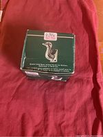 Photo of the green box showing the brass bird hook product and brand Kitchen Rattlers, with labeling and text indicating use in kitchen, bathroom, or bedroom.