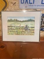 Full view of framed watercolor painting showing a landscape with wooden fence, cattails, grasses, and trees in the distance.