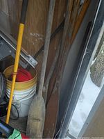 Photo showing several old wooden paddles leaning against a wall with some buckets nearby.