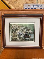 Overall view of framed print depicting two ducks near rocks in water.