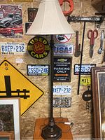 Full view of the standing floor lamp with beige shade against a wall with vintage license plates and signs.
