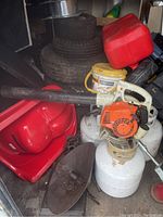 Image showing orange and white Stihl gas leaf blower with a black air tube, surrounded by various other equipment and objects.