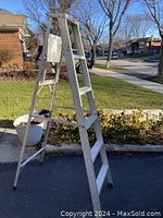 Full side angled view of the aluminum step ladder outdoors on pavement showing its structure and condition.
