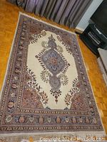 Full view of the rectangular area rug on hardwood floor showing sky blue center medallion and cream field with floral borders in shades of red, blue, and brown.