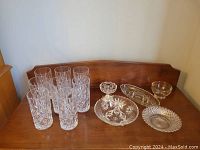 Full view of six crystal drinking glasses and five assorted decorative crystal bowls and dishes arranged on a wooden surface.