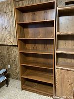Full view of the tall wooden bookshelf with six shelves in a room with wooden panel walls.