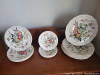 Group photo of all 15 plates grouped by size showing floral patterns and scalloped edges.