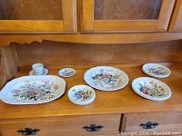 Full set on wooden cabinet showing platter, plates, cup and saucer with floral design.