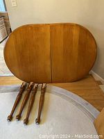 Large oval solid oak dining table laid on side with four separate legs and one leaf visible