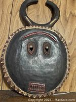 Front view of the metal wildebeast mask showing detailed facial features, horns, and geometric border.