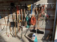 Photo showing front wall with hanging garden tools including rakes, shovels, hoes, extension cords and pruning tools organized on hooks.